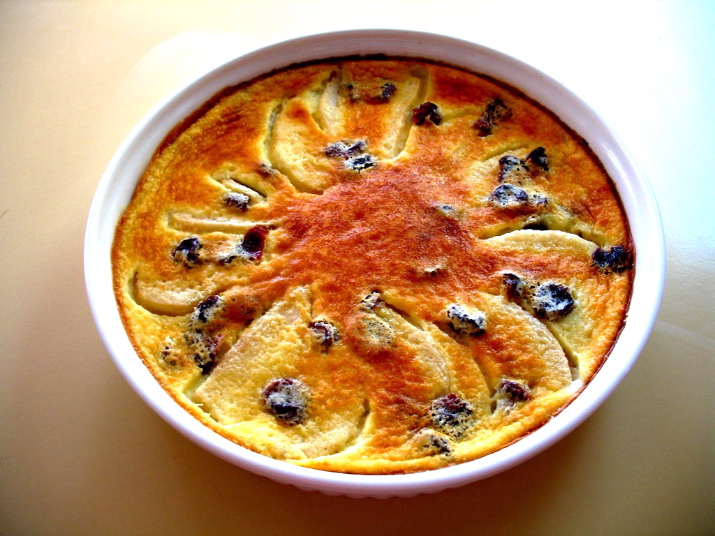 Pear and dried cherry clafouti in a round baking dish, dusted with confectioner’s sugar and photographed just after baking.