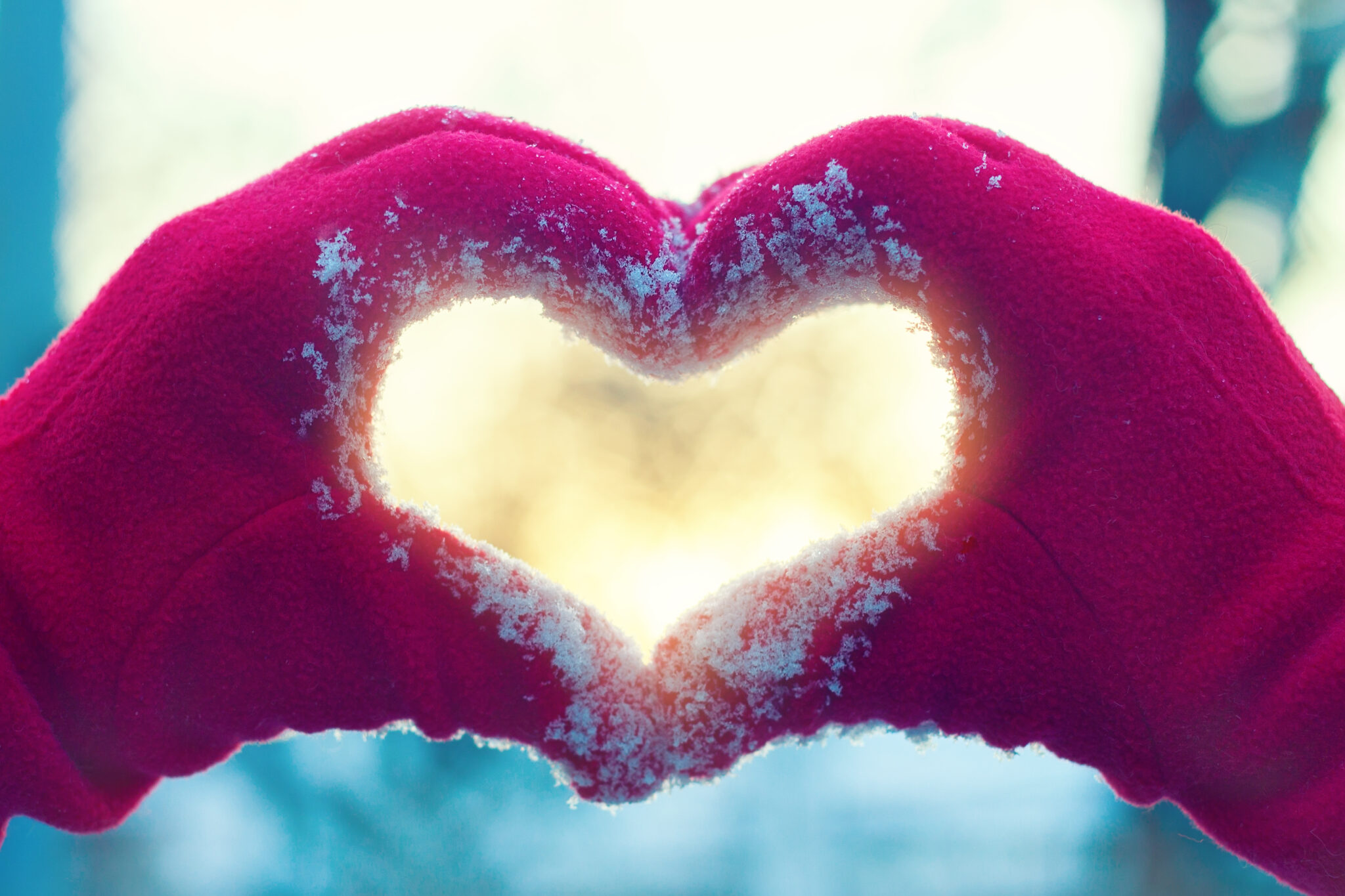 Red-gloved hands forming a heart shape in fresh snow, symbolizing holiday giving and community support.