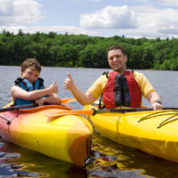 Parent and child kayaking together on a calm lake, wearing life jackets