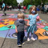 two kids in masks standing on street mural