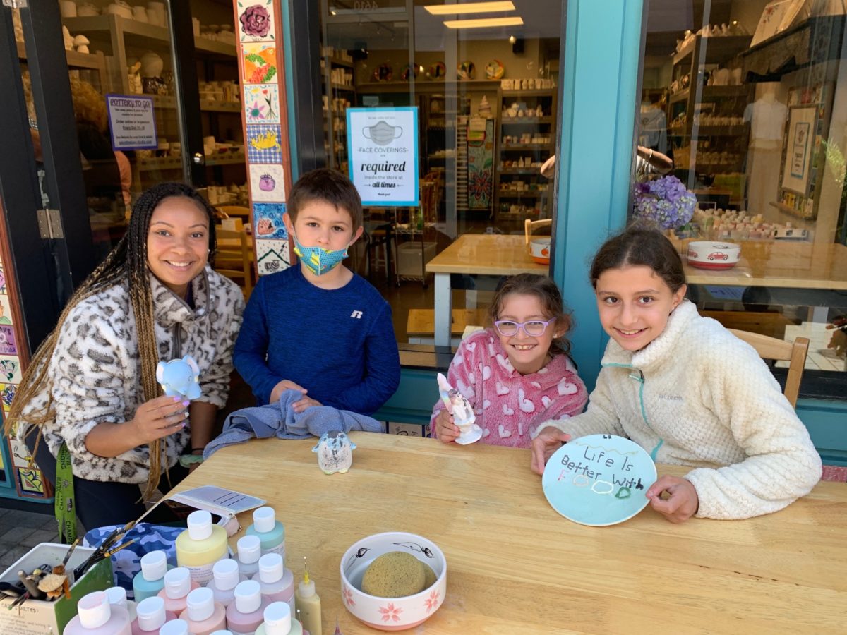 Pottery painting: An adult and three kids show off their creations at the Paint The Town outdoor table