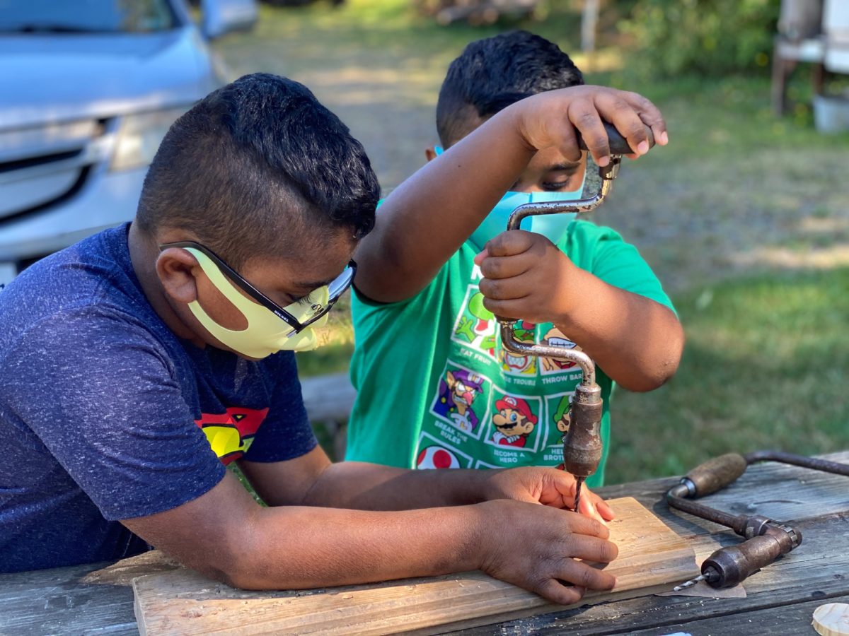 Day trip: boy helps his younger brother with a hand drill