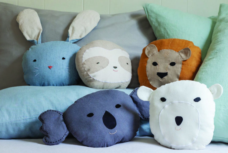 Handmade lion pillows and panda bath puppets from “Animal Friends to Sew,” arranged on a neatly made bed as inspiration for kid-friendly DIY sewing gifts.