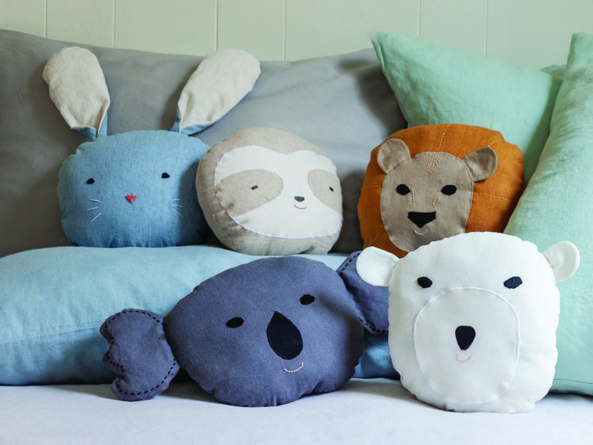 Handmade lion pillows and panda bath puppets from “Animal Friends to Sew,” arranged on a neatly made bed as inspiration for kid-friendly DIY sewing gifts.