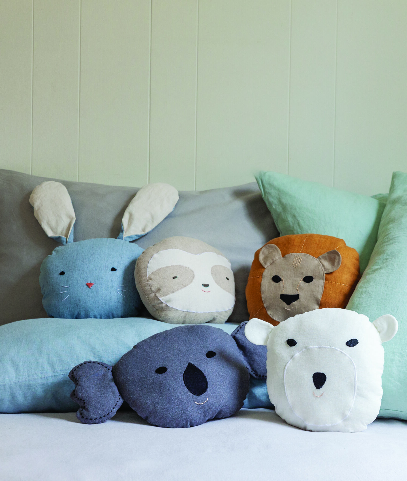 Handmade lion pillows and panda bath puppets from “Animal Friends to Sew,” arranged on a neatly made bed as inspiration for kid-friendly DIY sewing gifts.
