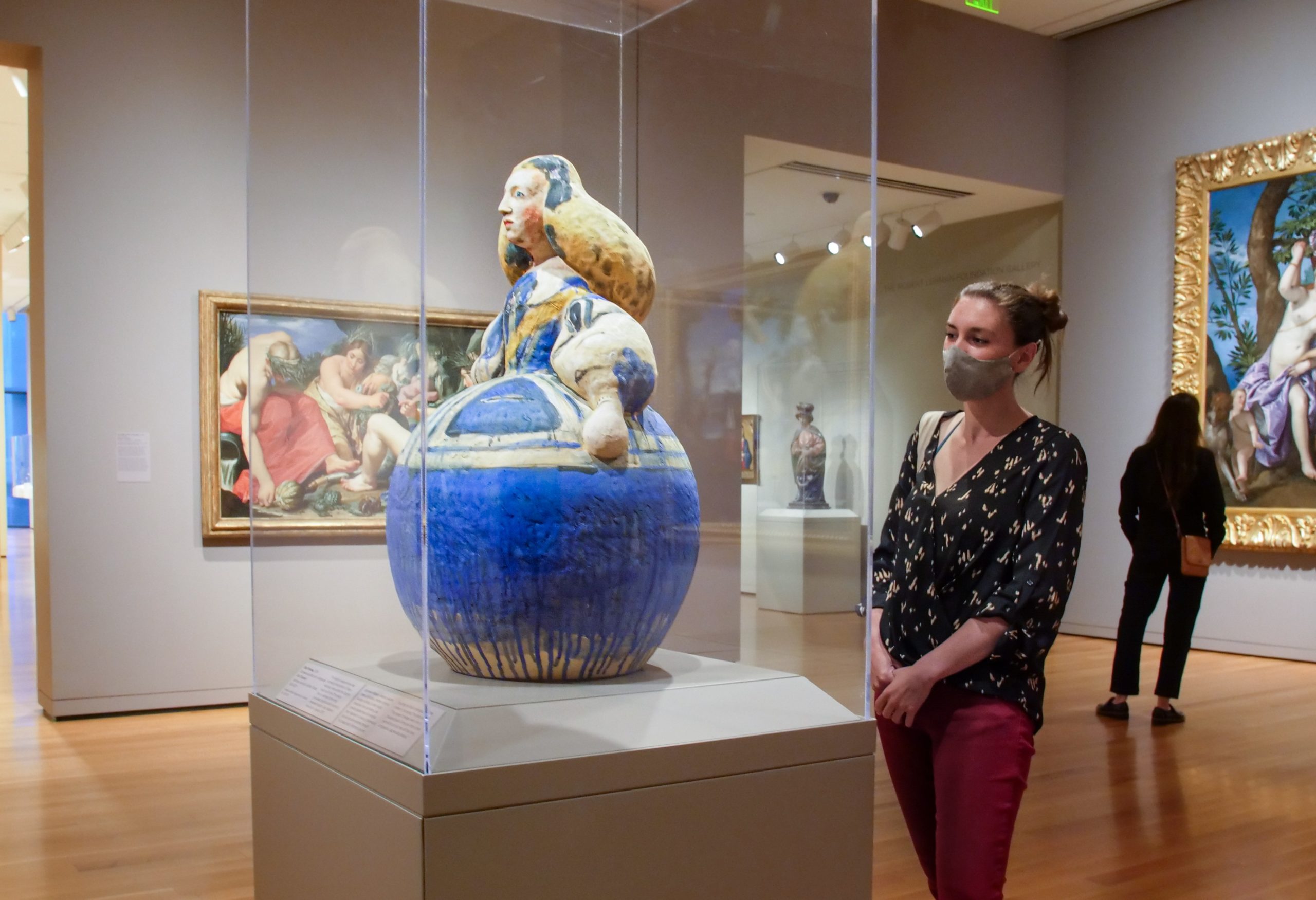Masked visitor observing a sculpture encased in glass at the Seattle Art Museum