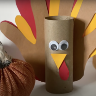 3-D Thanksgiving turkey craft made from a toilet paper roll with paper handprint feathers, googly eyes, and a small paper beak.