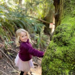 Little girl in the middle of a hiking trail, smiling at camera.