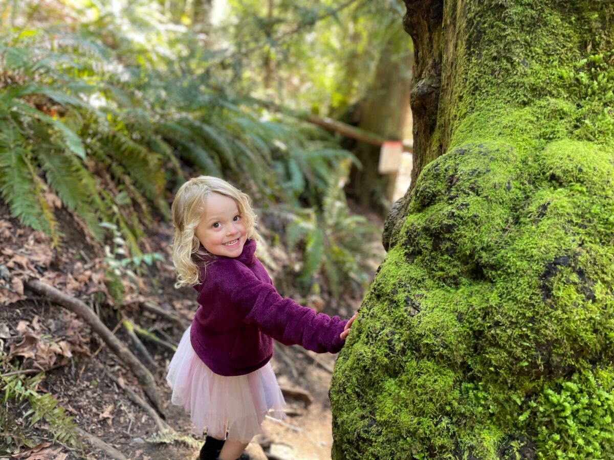 Little girl in the middle of a hiking trail, smiling at camera.