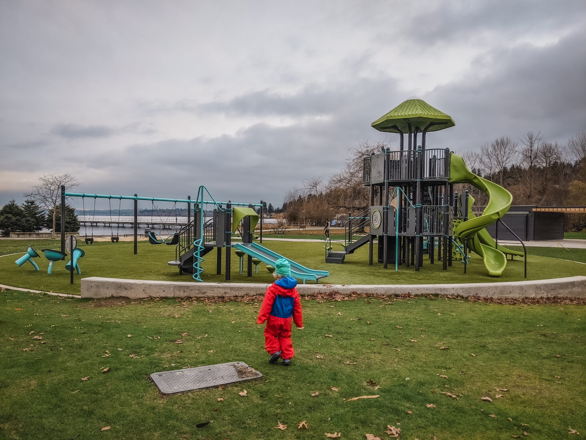 Little kid in rain gear runs towards large play scape area