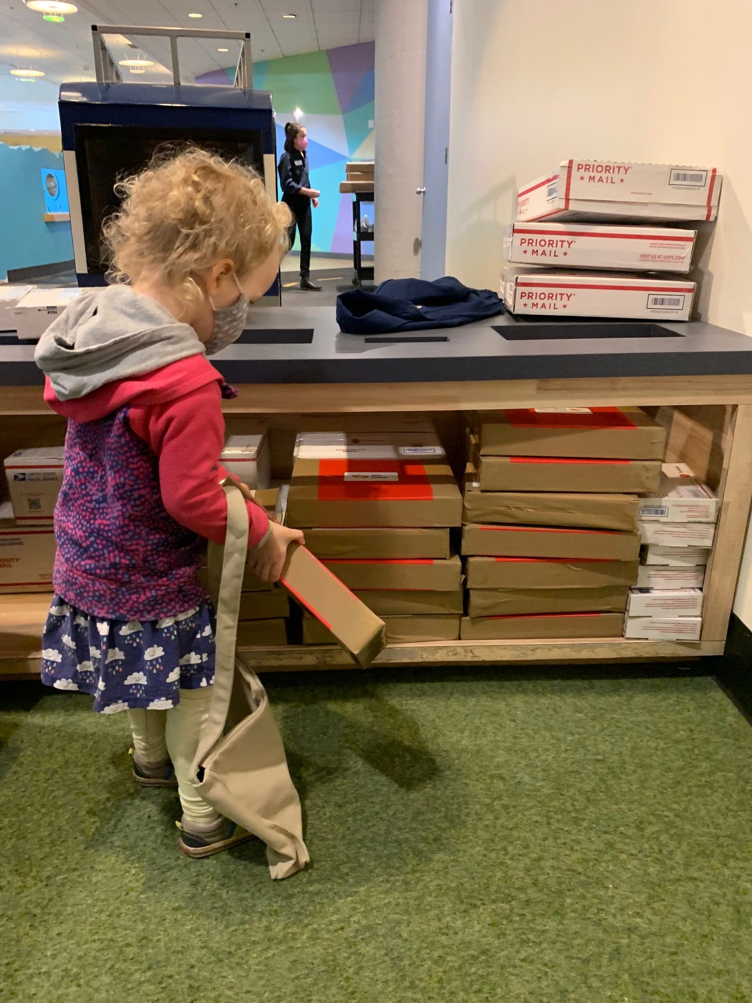 A young girl stacks postal boxes at the pretend post office.