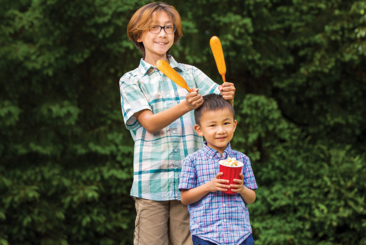 Two kids smiling and holding fair food at a summer fair