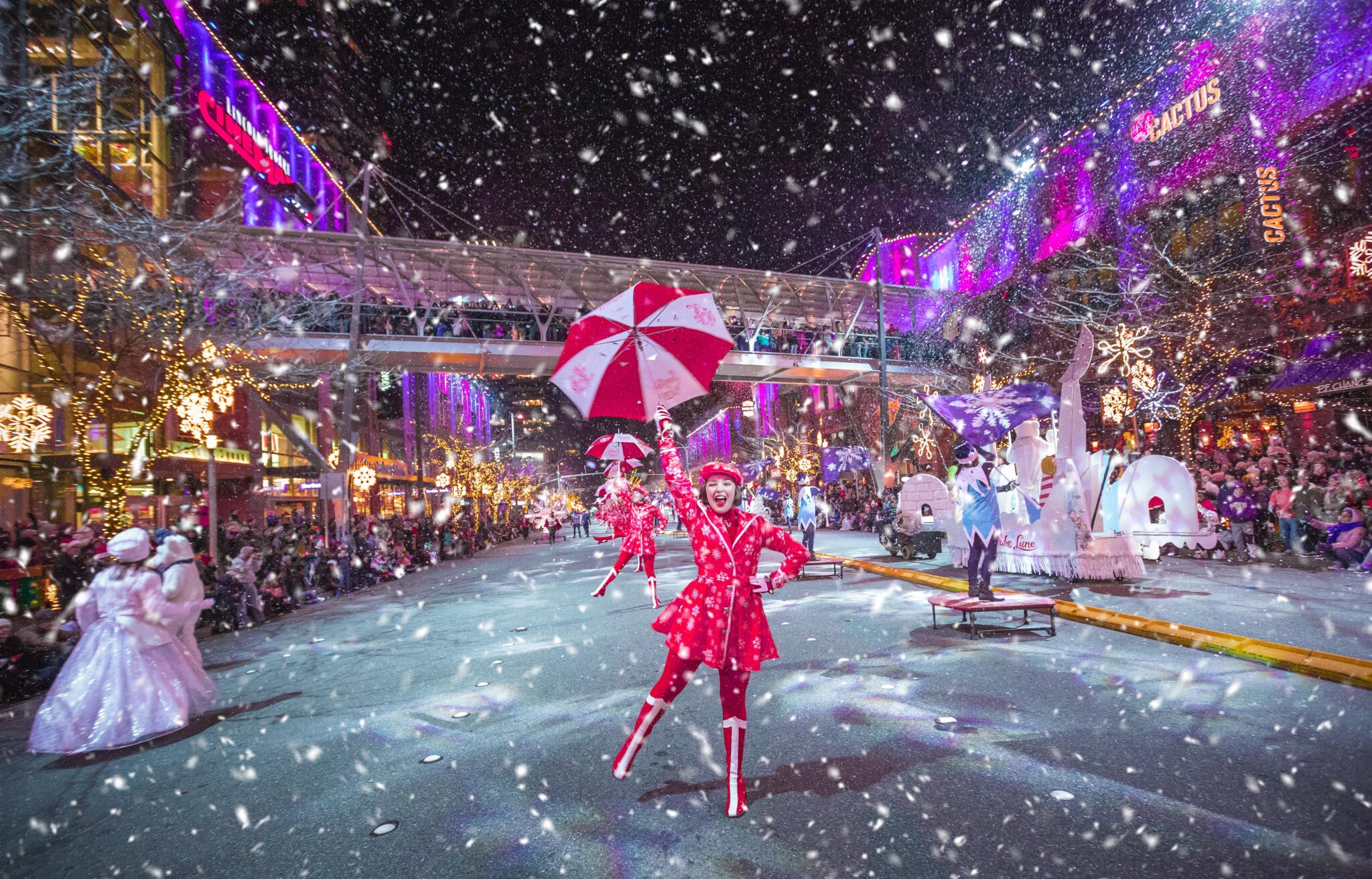 Snowflake Lane performer dancing along Bellevue Way in Bellevue, surrounded by lights, holiday decorations, and falling snow.