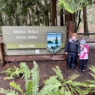 Two kids stand in front of state parks sign that says Bridle Trails