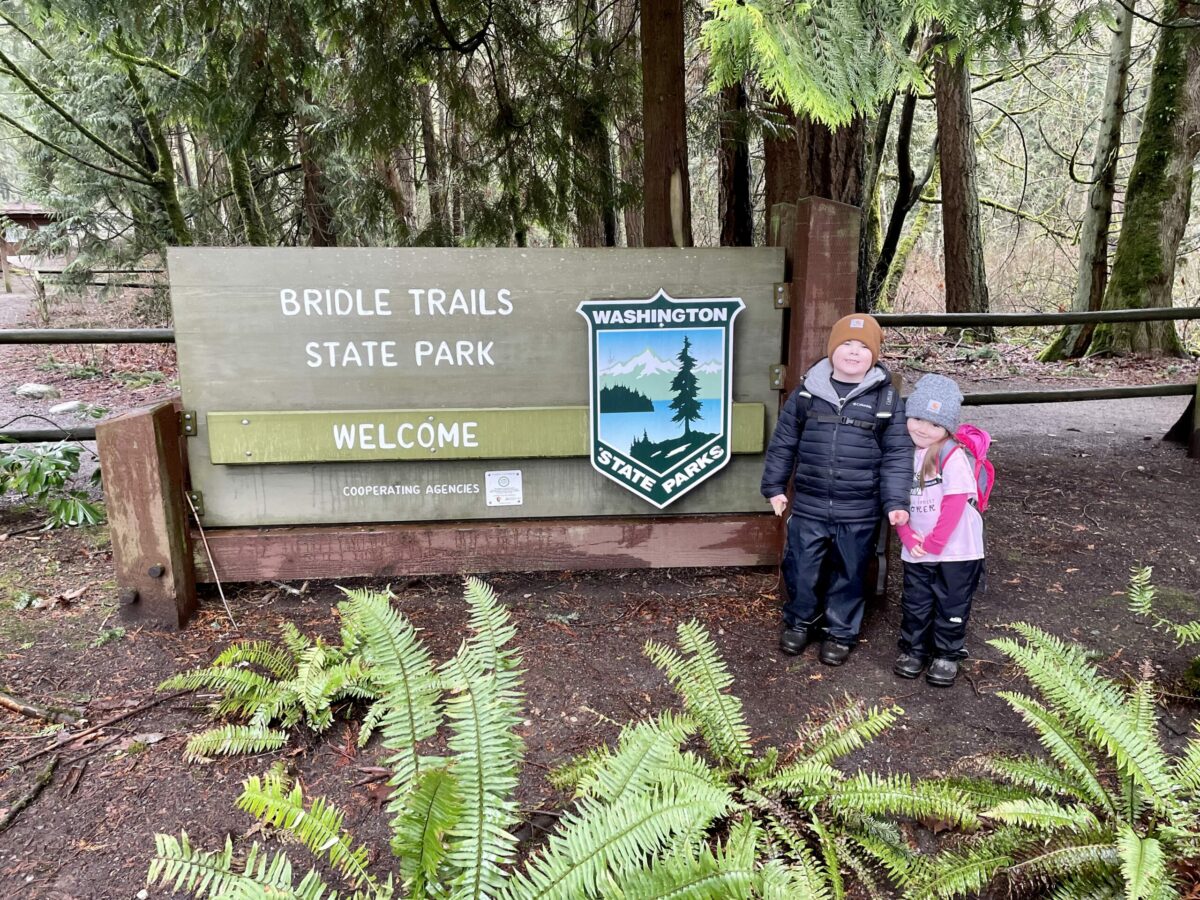Two kids stand in front of state parks sign that says Bridle Trails