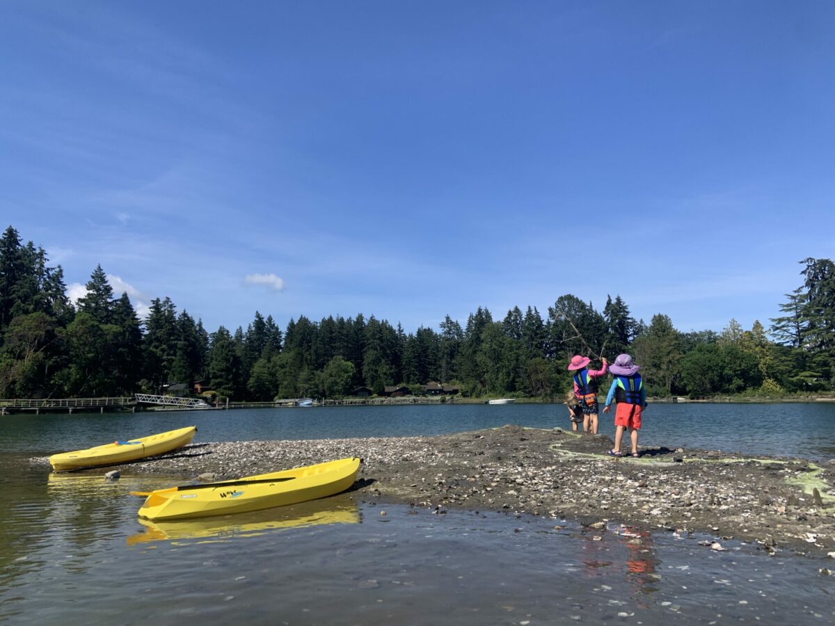 Two kids playing on a beach near colorful kayaks during a family paddling outing