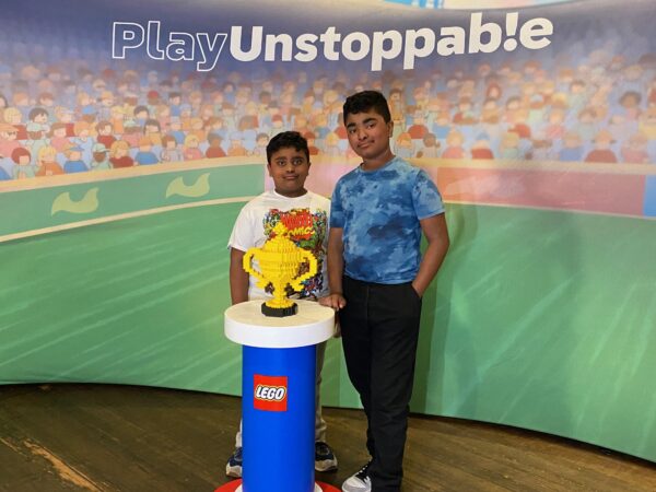two kids standing in front of soccer poster and a trophy made out of LEGO