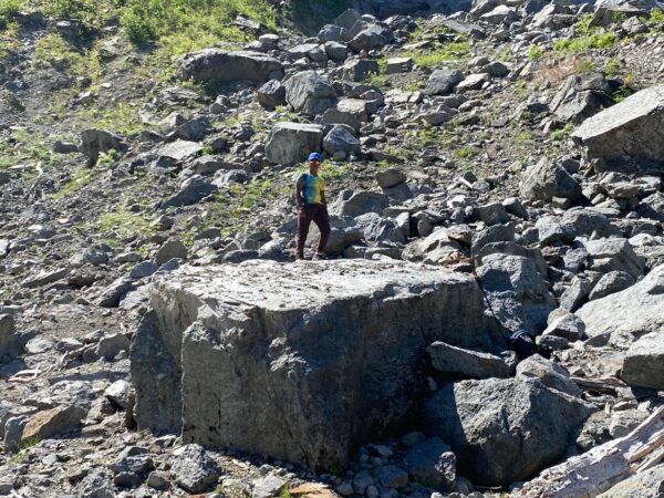 Two kids standing on a large boulder near the Big Four Ice Caves, surrounded by rocky terrain.