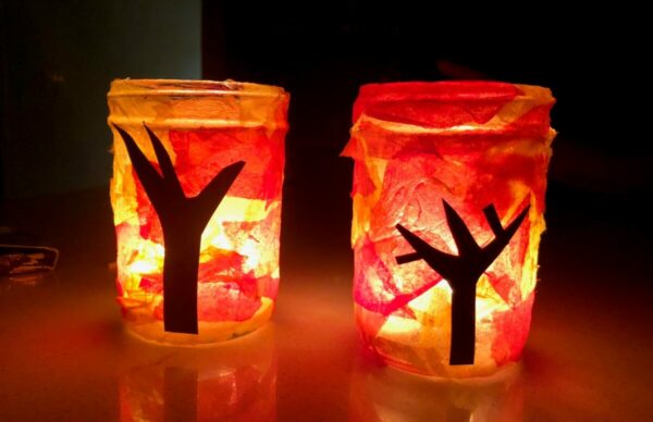 Colorful tissue paper lantern crafts glowing with warm light, made by kids during a fall art project at home.