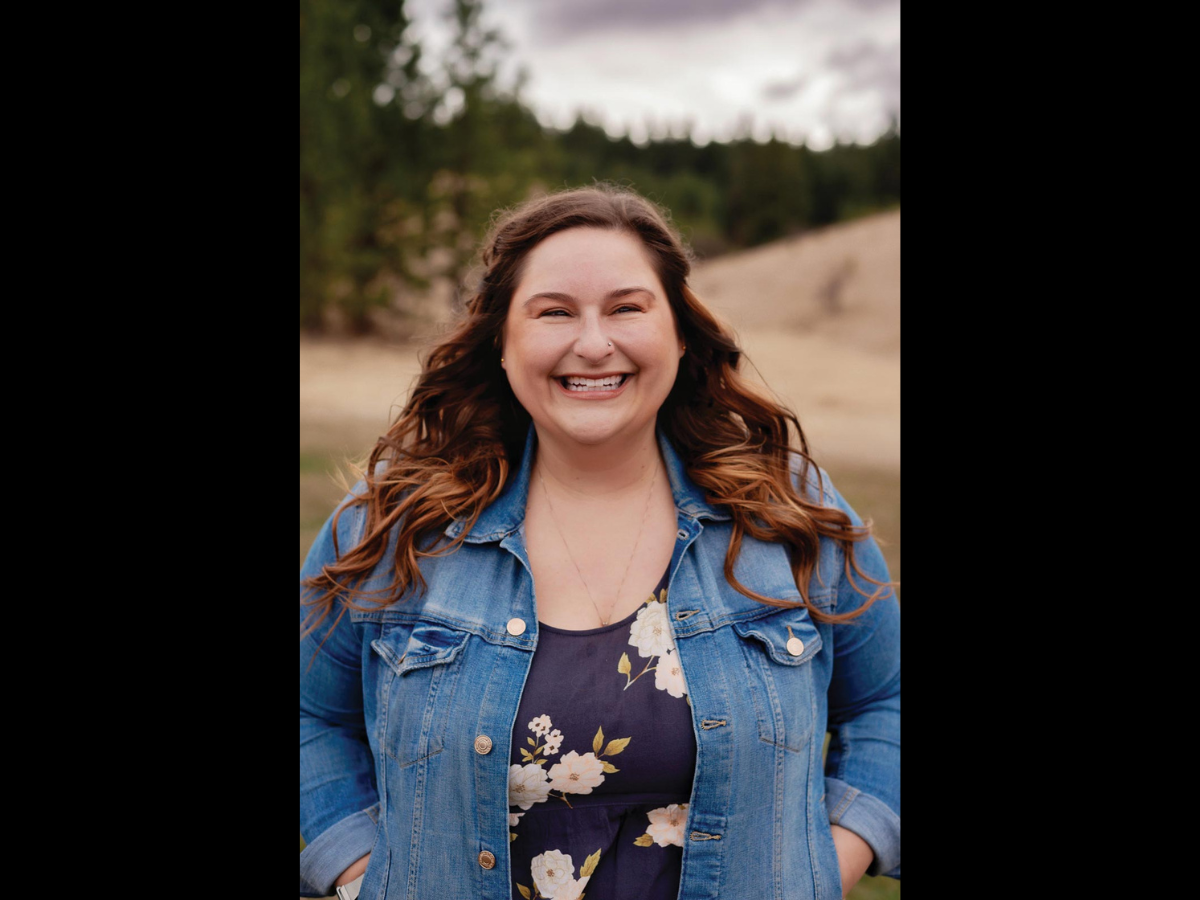 Headshot of a woman with brown wavy hair, wearing a navy floral blouse and jean jacket.