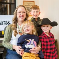 Woman sits at office desk with computer in the background, surrounded by three child.