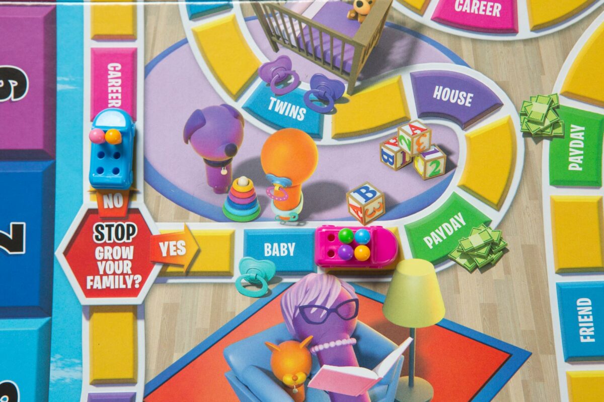 Close up of a board game spoofing the Life game, with stops along the way like "Stop! Grow your family?" and "Baby" "Payday" "House" "Twins" and "Career".