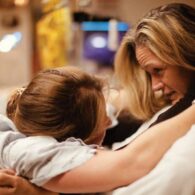 Woman in labor leans forward to hold onto another woman, her midwife. They are looking each other in the eye and holding tightly.