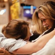 Woman in labor leans forward to hold onto another woman, her midwife. They are looking each other in the eye and holding tightly.
