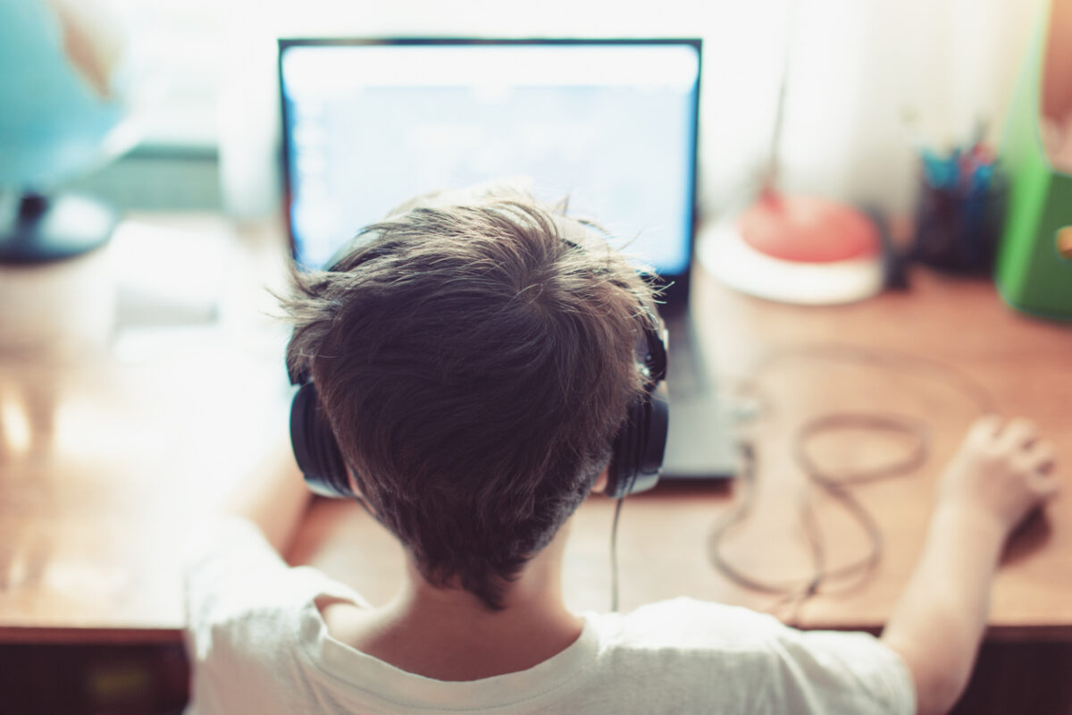 Back of child's head, with headphone on facing a computer screen at a desk