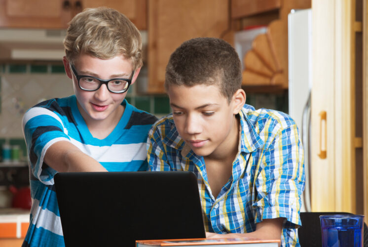 Two male teen friends in kitchen with books and laptop