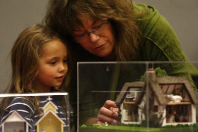 Woman and child point at miniature house and garden exhibit. Child's face is in wonder.