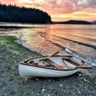Row boat is moored on the beach, with a gorgeous orange and yellow sunset behind it against the water.