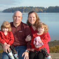 Woman, man and two children sit posed for a family photo on a beach.