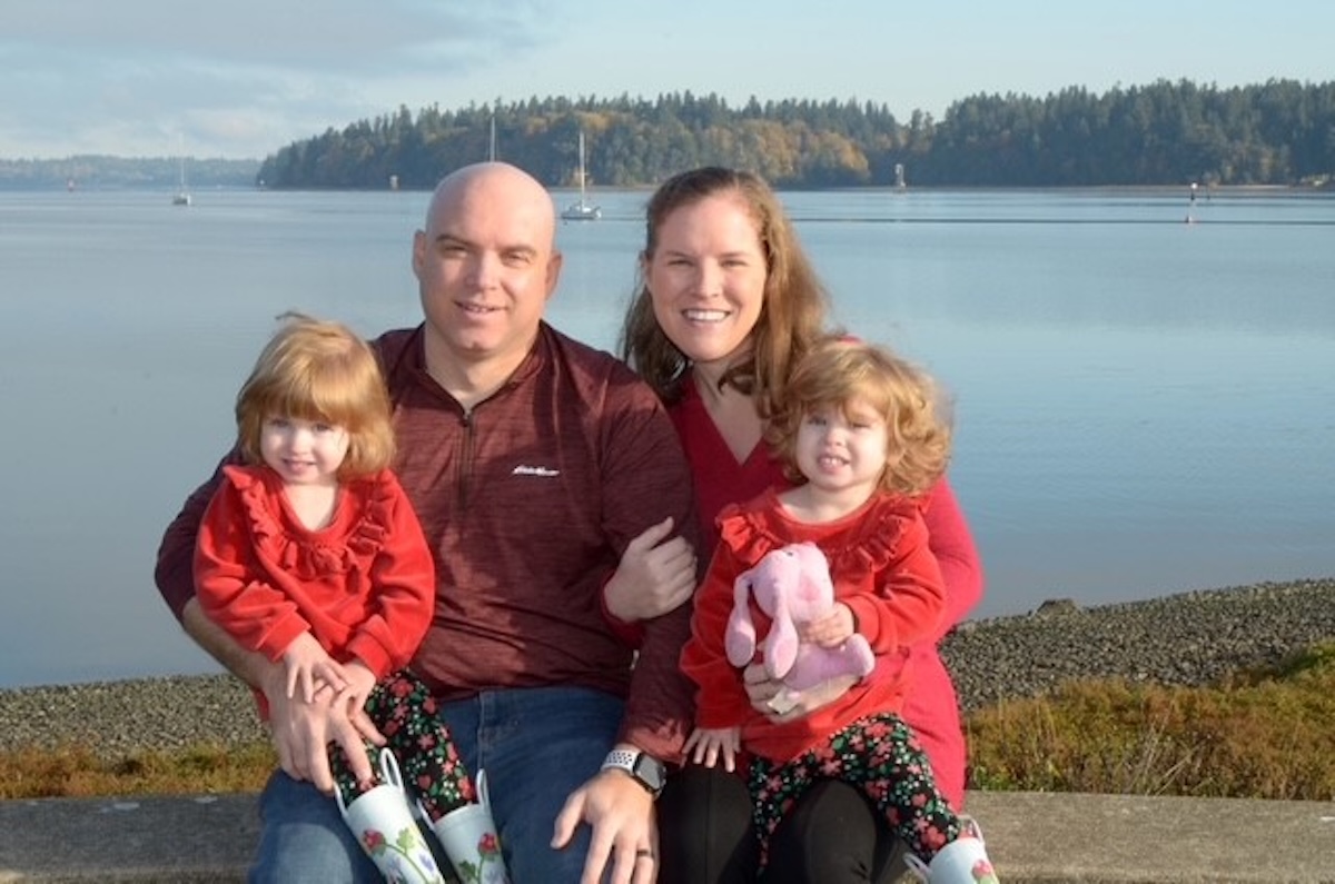 Woman, man and two children sit posed for a family photo on a beach.