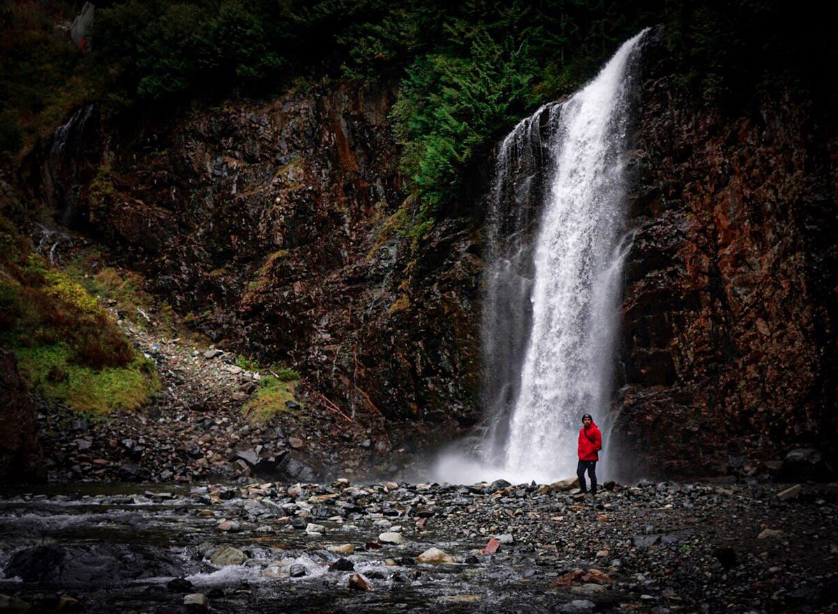 Franklin Falls in with Jonathan Gulingan standing in the foreground. The waterfall is full and crashing into the rocks.