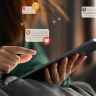 Close up of a hand touching a tablet, with Facebook likes and heart graphics surrounding the screen indicating social media use.