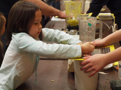 Little girls pressing her hands down on a piece of paper she has glued something to, making an art project.