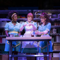 Three actresses in waitress uniforms stand baking a pie