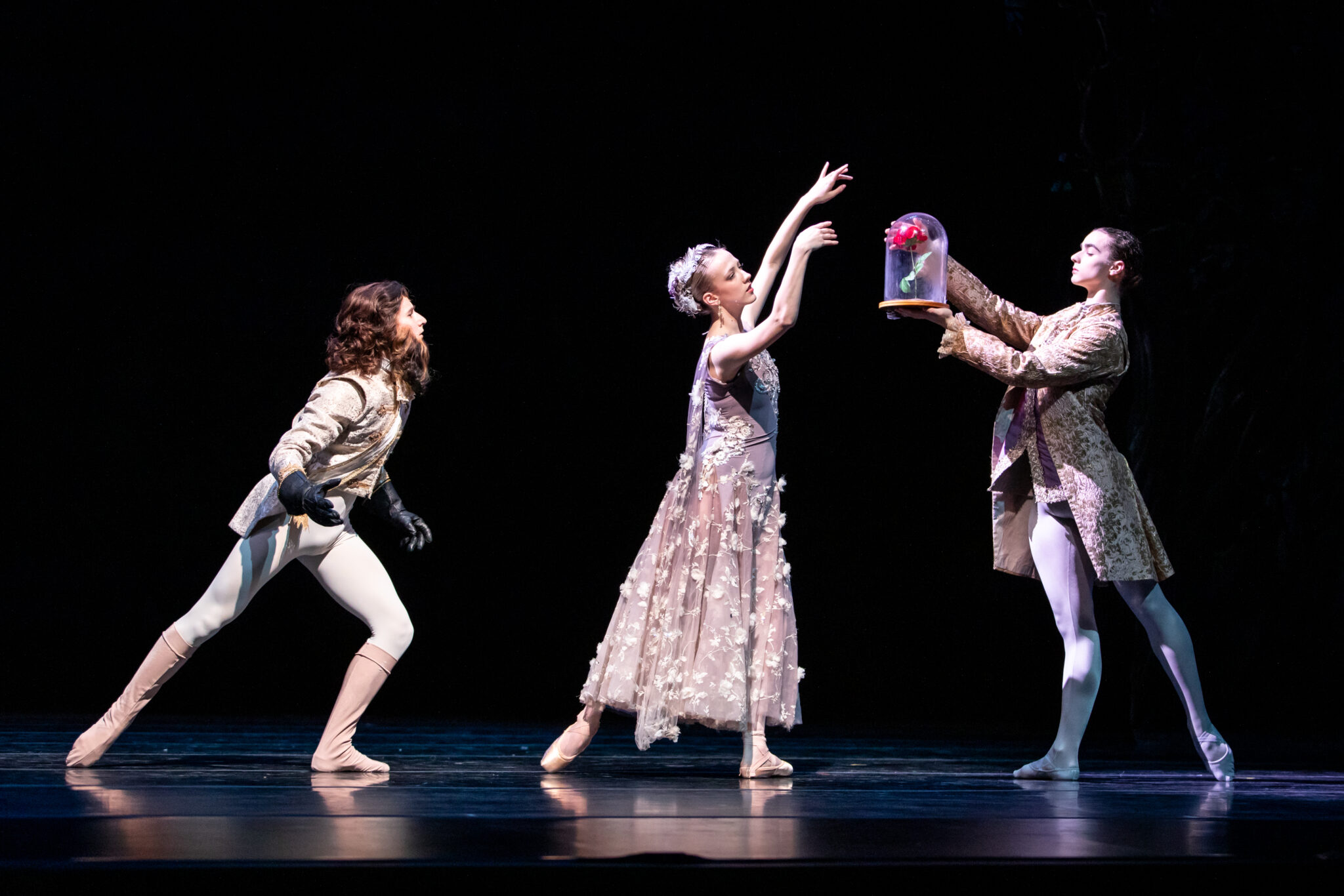 Dancers on stage hold rose encased in glass
