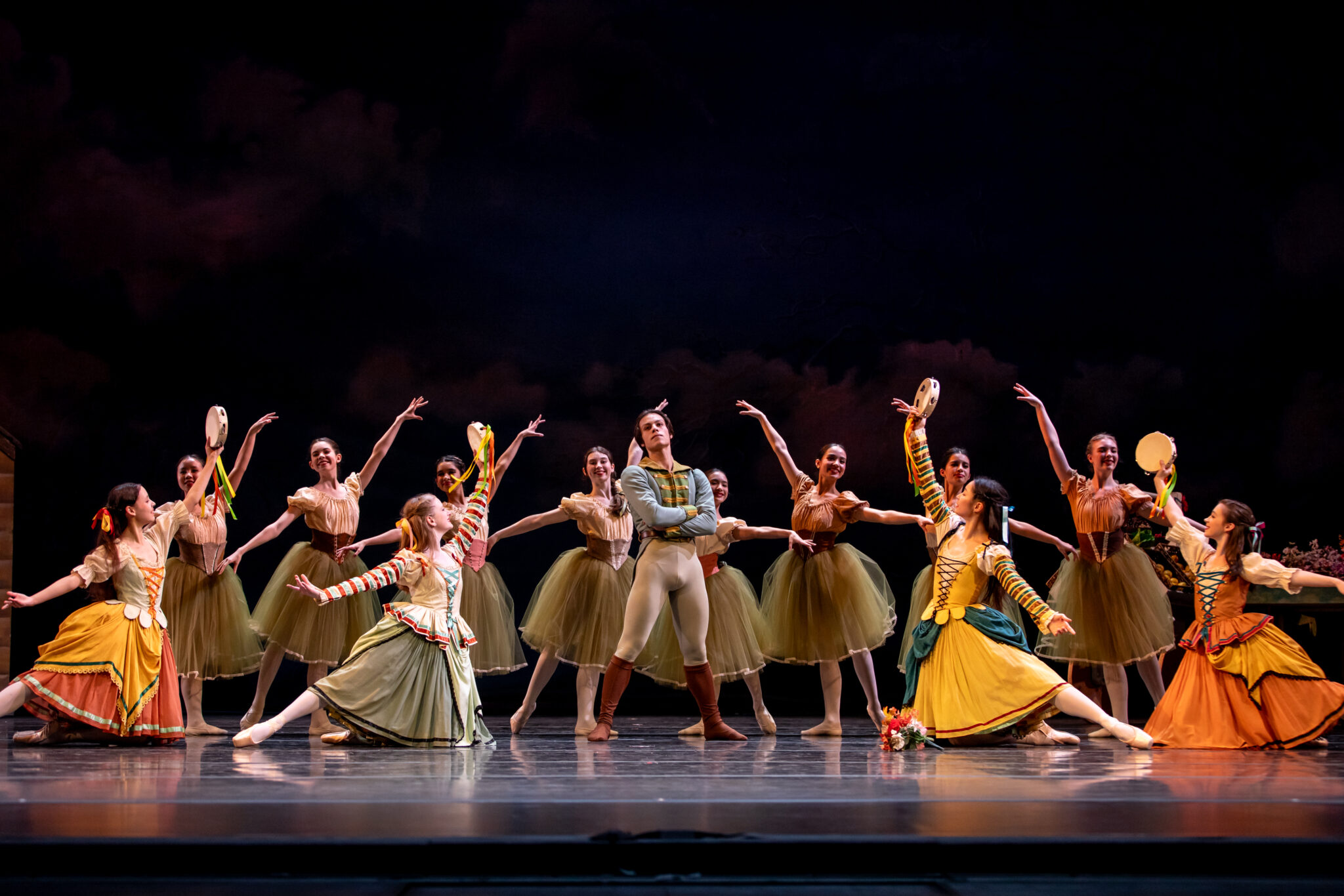 Numerous female dancers pose around single male dancer, Gaston