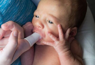 baby sucking on an adult's finger
