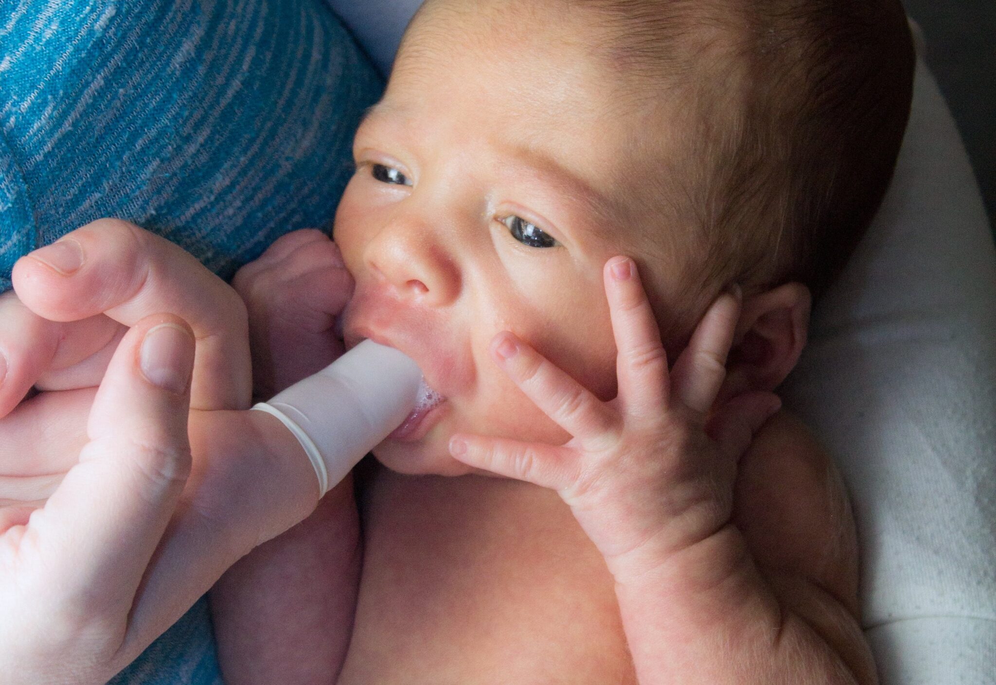 baby sucking on an adult's finger