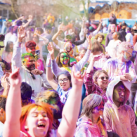 Crowd of people with their hands up covered in colored dust.