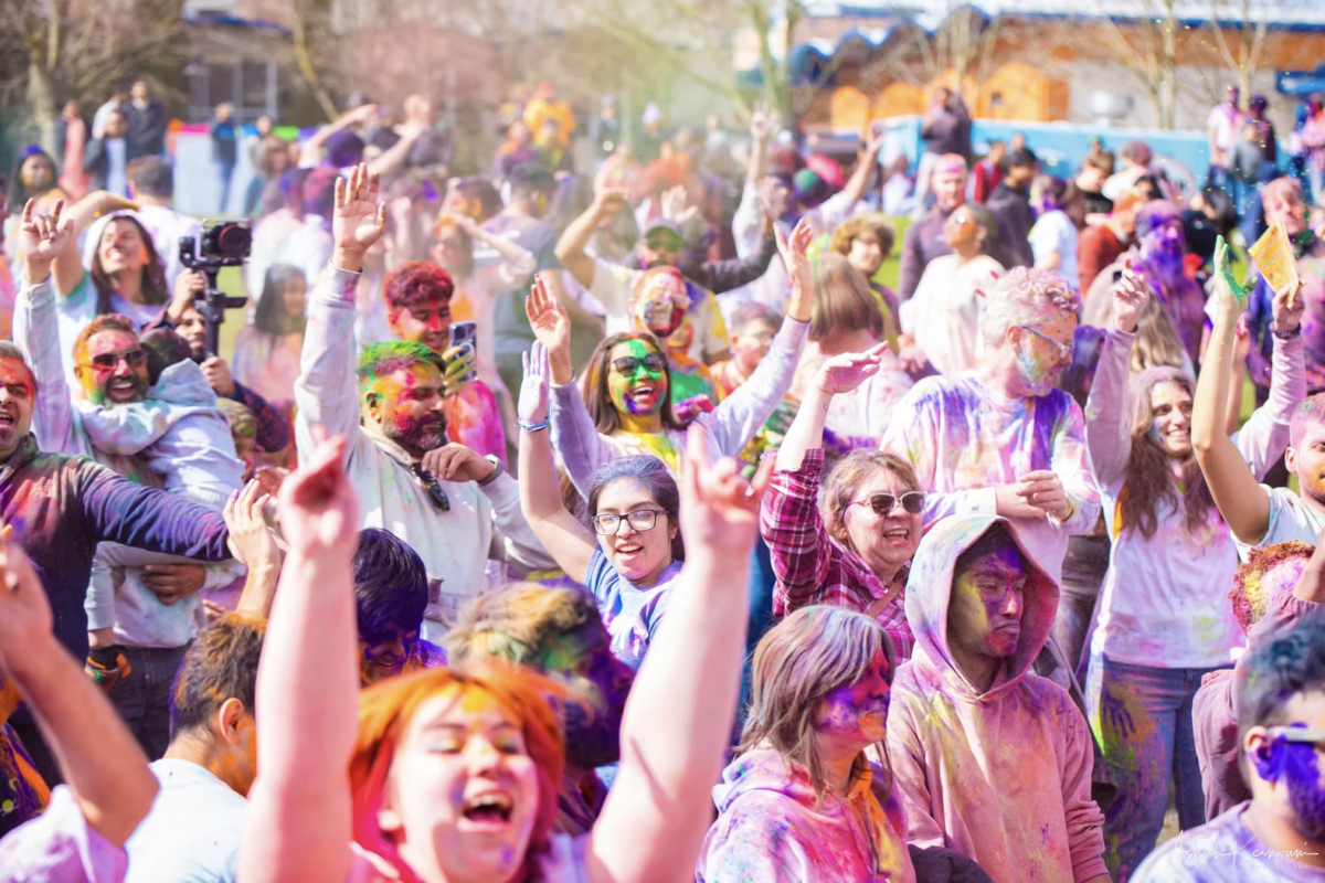 Crowd of people with their hands up covered in colored dust.