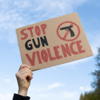 Hand holding a sign with slogan Stop Gun Violence and black pistol strikethrough. Woman with placard at protest rally demonstration strike to ban weapons and end shooting.