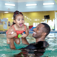 Adult holds smiling child up in pool