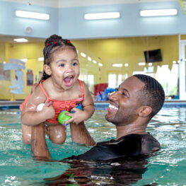 Adult holds smiling child up in pool