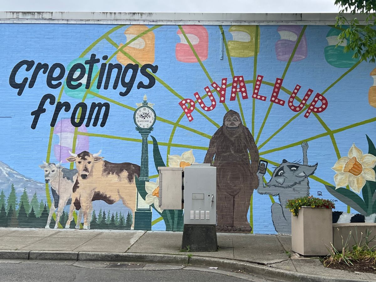 Mural that says "Greetings from Puyallup" with cows, flowers and Big Foot on it.