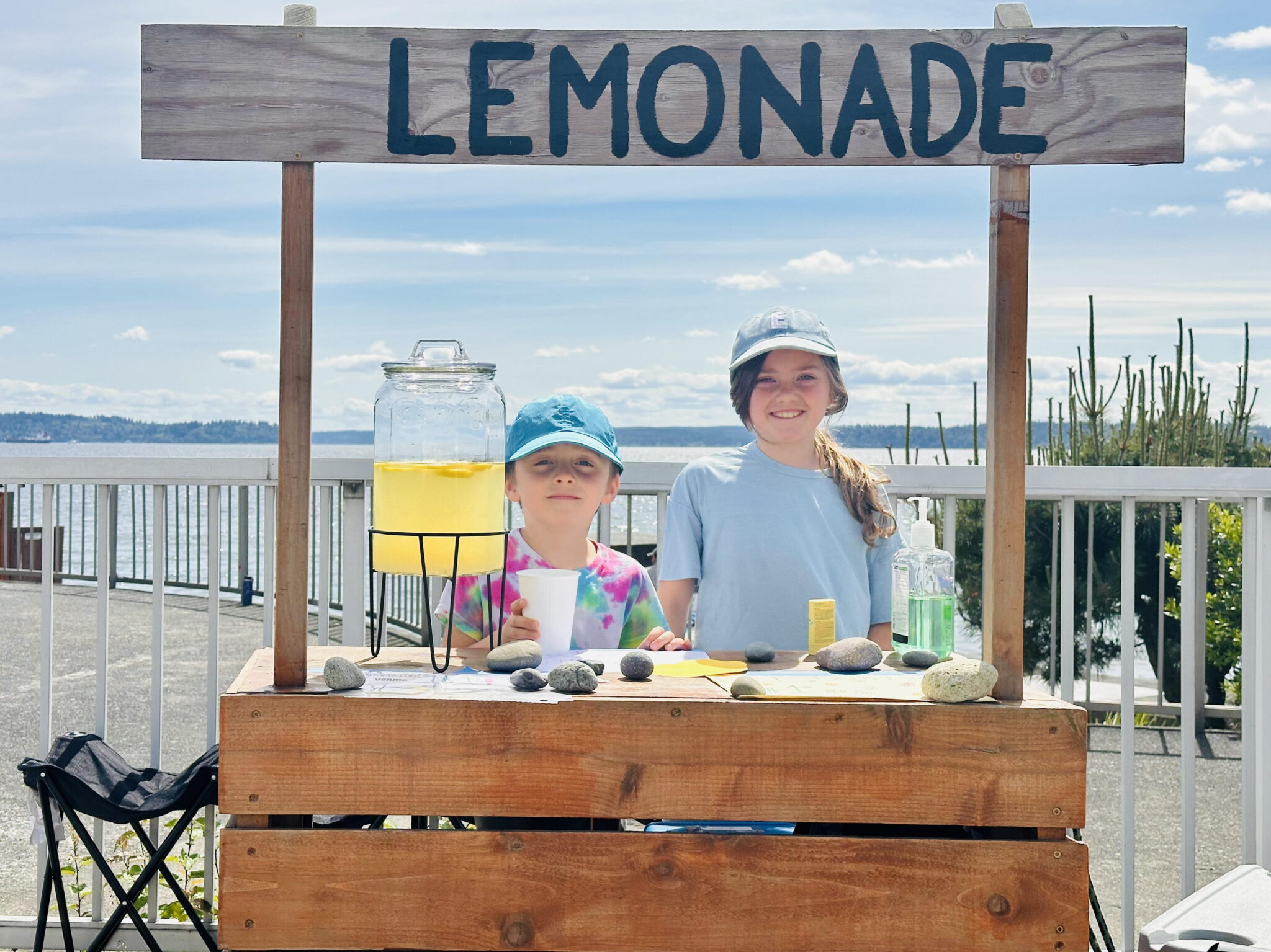 Etta, 10, and Hugo, 8, run a homemade lemonade stand, continuing a family tradition with the same wooden stand their dad used as a child.