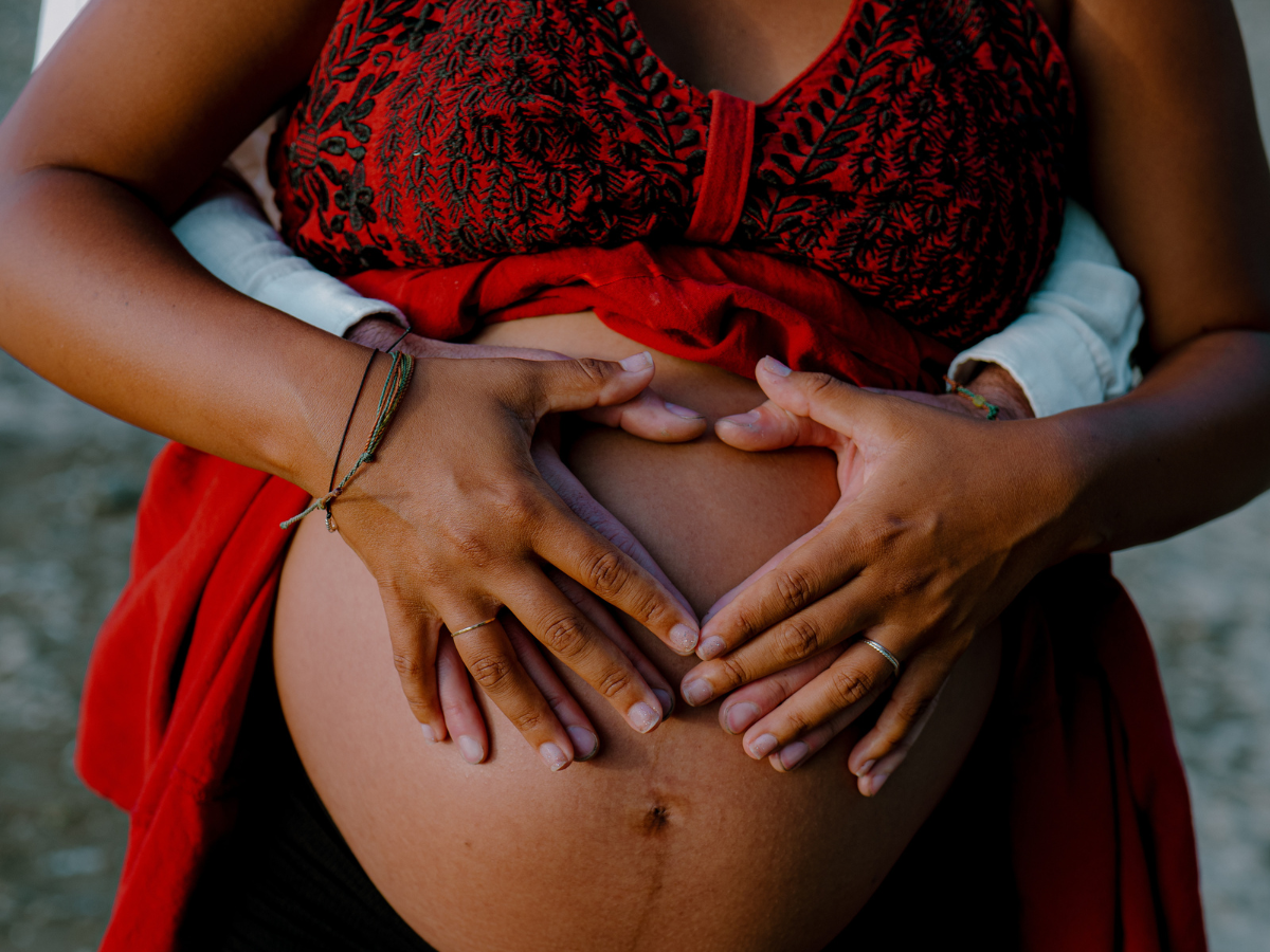 Close-up of four hands cradling a pregnant belly, symbolizing family connection, support, and generational love.